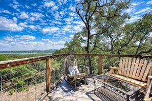 An outdoor deck with a wicker chair and a wooden bench, overlooking a forested landscape.
