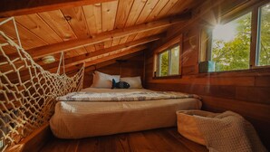 Una habitación de cabaña de madera con una cama, una ventana y una hamaca de cuerda.