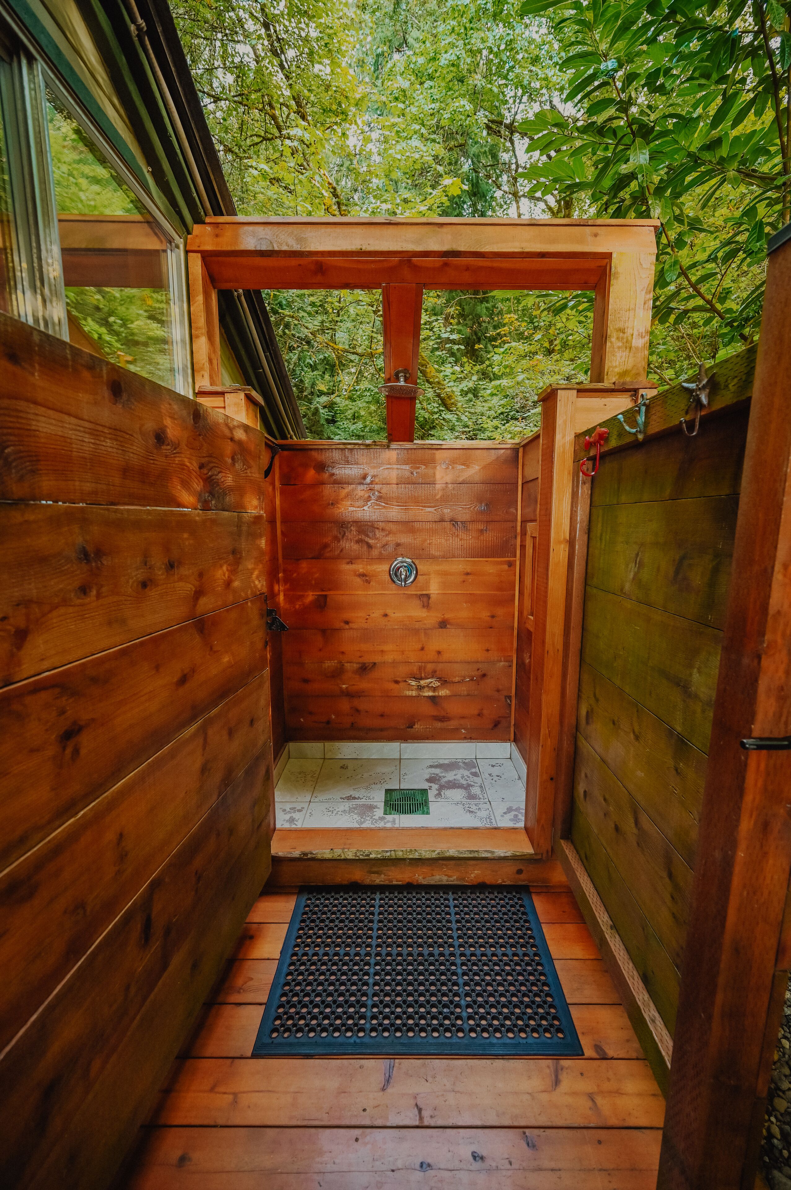 A wooden shower enclosure with a metal grate floor, surrounded by wooden walls and a glass door.