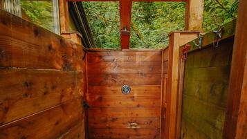 A wooden shower enclosure with a metal grate floor, surrounded by wooden walls and a glass door.