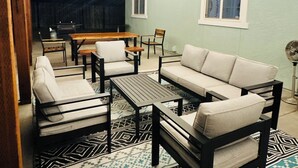 An outdoor patio area with a wooden ceiling, string lights, a sofa, chairs, a table, and a patterned rug. - Wendover's most comfortable house for rent. (West Wendover)
