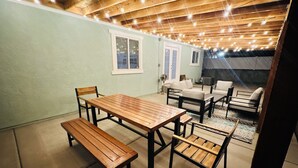 A covered patio with a wooden table and benches, surrounded by chairs and a sofa. - Wendover's most comfortable house for rent. (West Wendover)