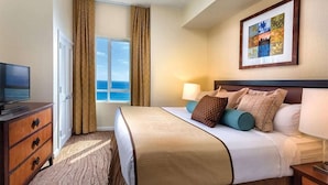 A hotel room with a bed, a TV, a dresser, a window with curtains, and a framed picture on the wall. - Club Wyndham Resort 3 Bedroom Presidential Ocean View (Oceanside)