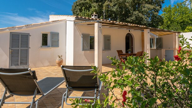 A covered outdoor seating area with two chairs and a table, a potted plant, and a view of a tree and sky. - Villa Les Oliveres Petites en Pollensa by Mallorca North Villas (Pollensa)