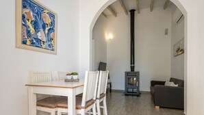 A living room with a white table, two white chairs, a grey sofa, a black fireplace, and a painting on the wall. - Villa Les Oliveres Petites en Pollensa by Mallorca North Villas (Pollensa)