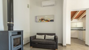A modern living room with a sofa, a fireplace, and a kitchen in the background. - Villa Les Oliveres Petites en Pollensa by Mallorca North Villas (Pollensa)
