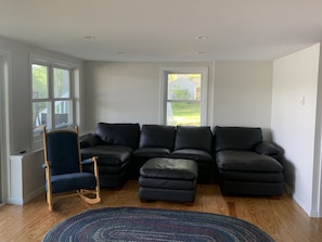 Relax in this inviting living room with a sofa and a rocking chair, offering a view of the outdoors through large windows.