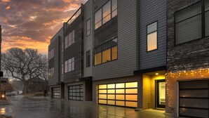 A modern multi-story building with large windows and garage doors, featuring a wet pavement and a sunset sky.