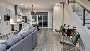 A modern kitchen with white cabinets, a grey sofa, and a dining area with a table and chairs.