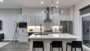 A modern kitchen with white cabinetry, a large island with bar stools, a built-in oven, and a stainless steel refrigerator.
