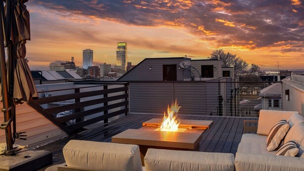 A rooftop terrace with a fire feature, seating, and a city skyline view.