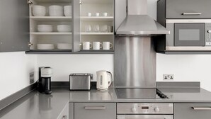 A modern kitchen with stainless steel appliances, including a microwave, toaster, and coffee maker, and a cabinet with dishes and cups. - Hip Islington 2BR w/ Day Porter & Balcony, nr Kings Cross, by Blueground (London)