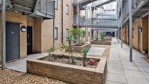 A courtyard with brick buildings, metal railings, and planters with small trees. - Hip Islington 2BR w/ Day Porter & Balcony, nr Kings Cross, by Blueground (London)