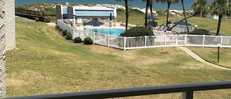 A pool area with a white fence, palm trees, and a view of the ocean.