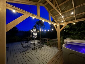 Une terrasse en bois avec un jacuzzi, des guirlandes lumineuses et une table avec des chaises.