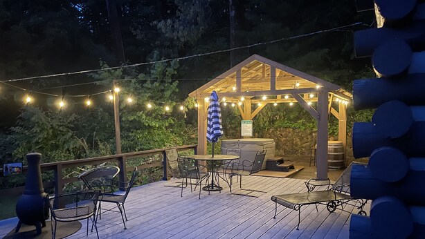 Terraza de madera con mobiliario exterior, bañera de hidromasaje y luces colgantes.