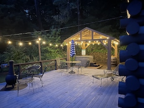 Eine Holzterrasse mit Sitzgelegenheit, Whirlpool und Lichterketten.