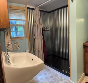 Une salle de bain avec un lavabo, une fenêtre, un rideau de douche et une porte en métal.
