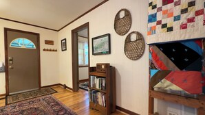 Un pasillo con suelo de madera, una puerta con ventanal, una estantería y un tapiz acolchado en la pared.