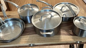 Una cocina con armarios de madera, una estufa y una mesa con varias ollas y sartenes de acero inoxidable.