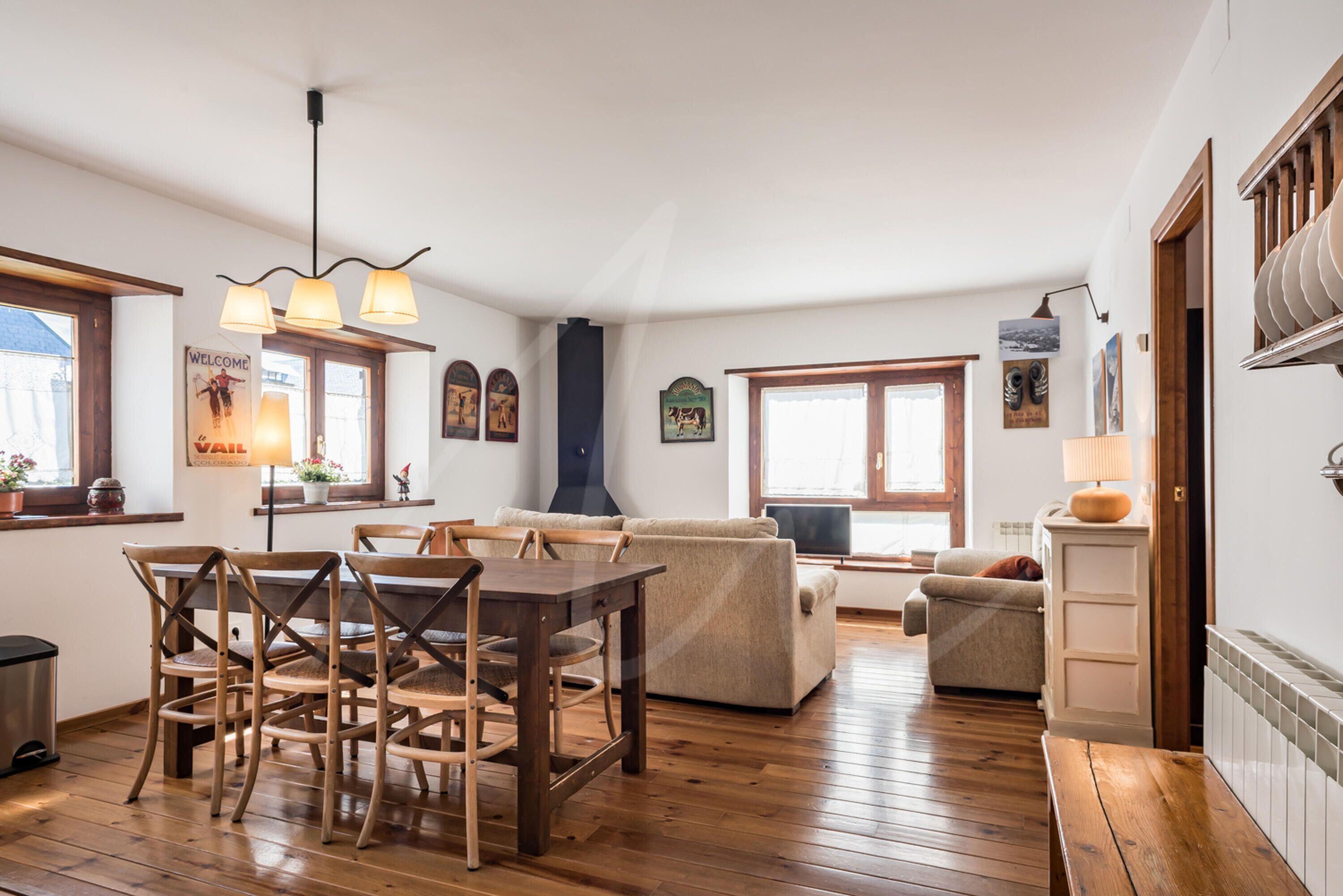 A spacious living area with a wooden dining table and chairs, a sofa, and a television.