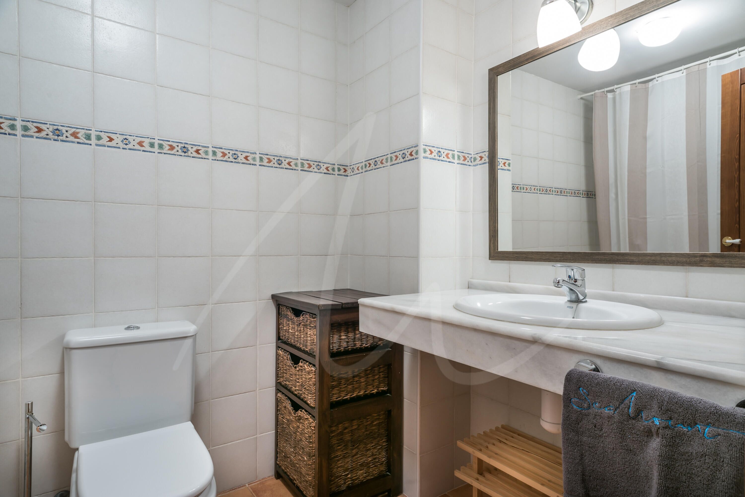 Ein Badezimmer mit Toilette, Waschbecken und Spiegel. Korbgeflechte und ein Handtuchhalter sind vorhanden.
