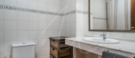 A bathroom with a toilet, a sink, and a mirror. There are wicker baskets and a towel rack.