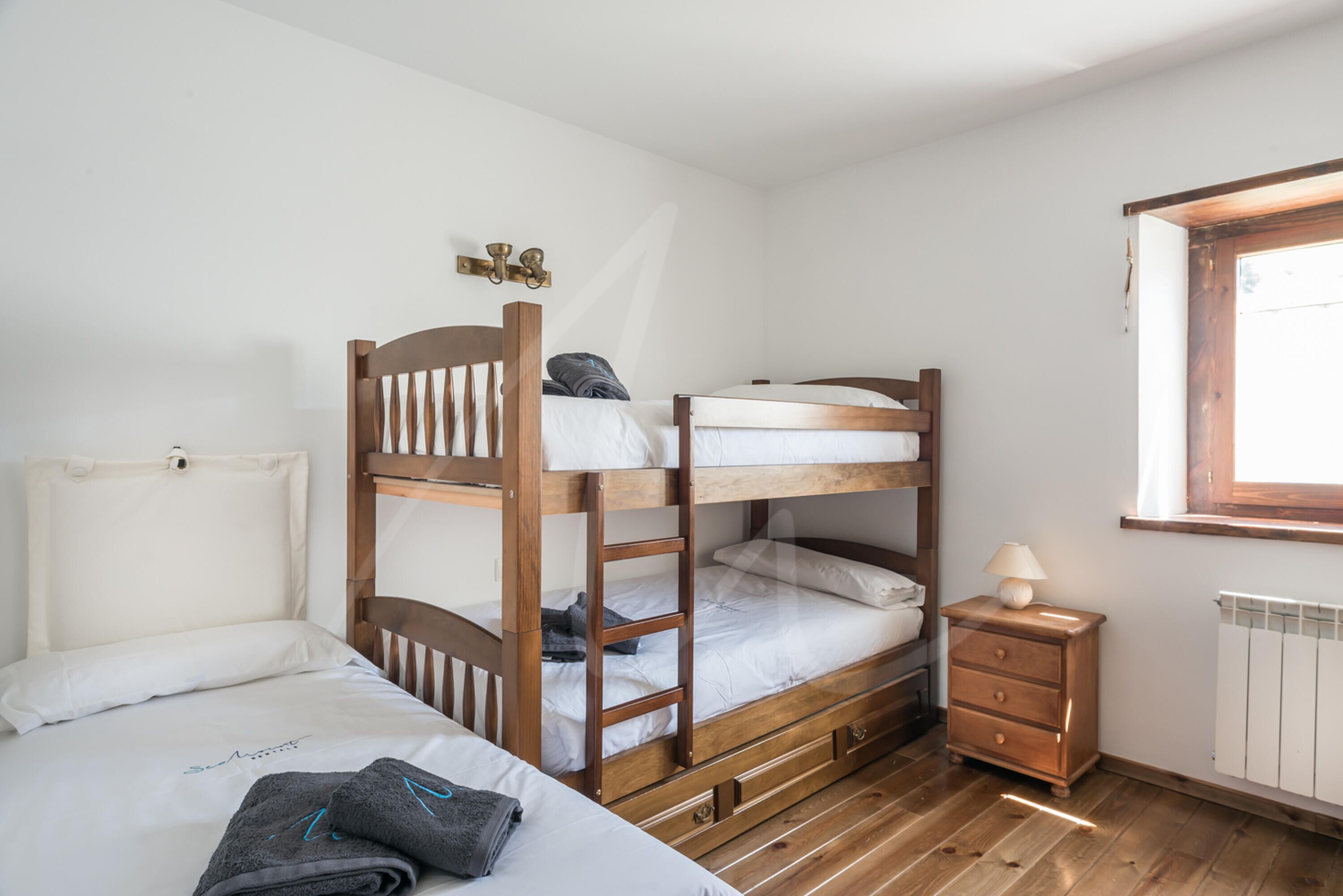 Une chambre avec un lit superposé, une échelle en bois, une table de chevet avec une lampe et une fenêtre avec des rideaux.