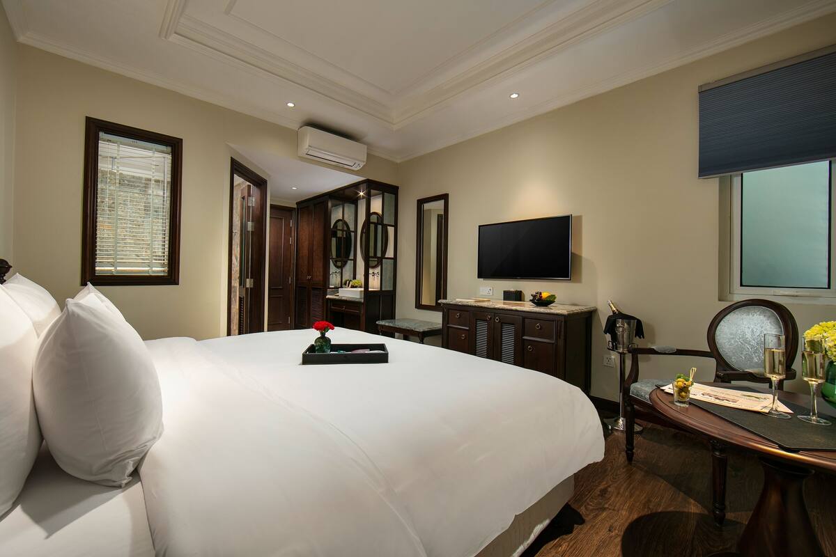 A hotel room with a large bed, a desk with a chair, a television, and an air conditioning unit.