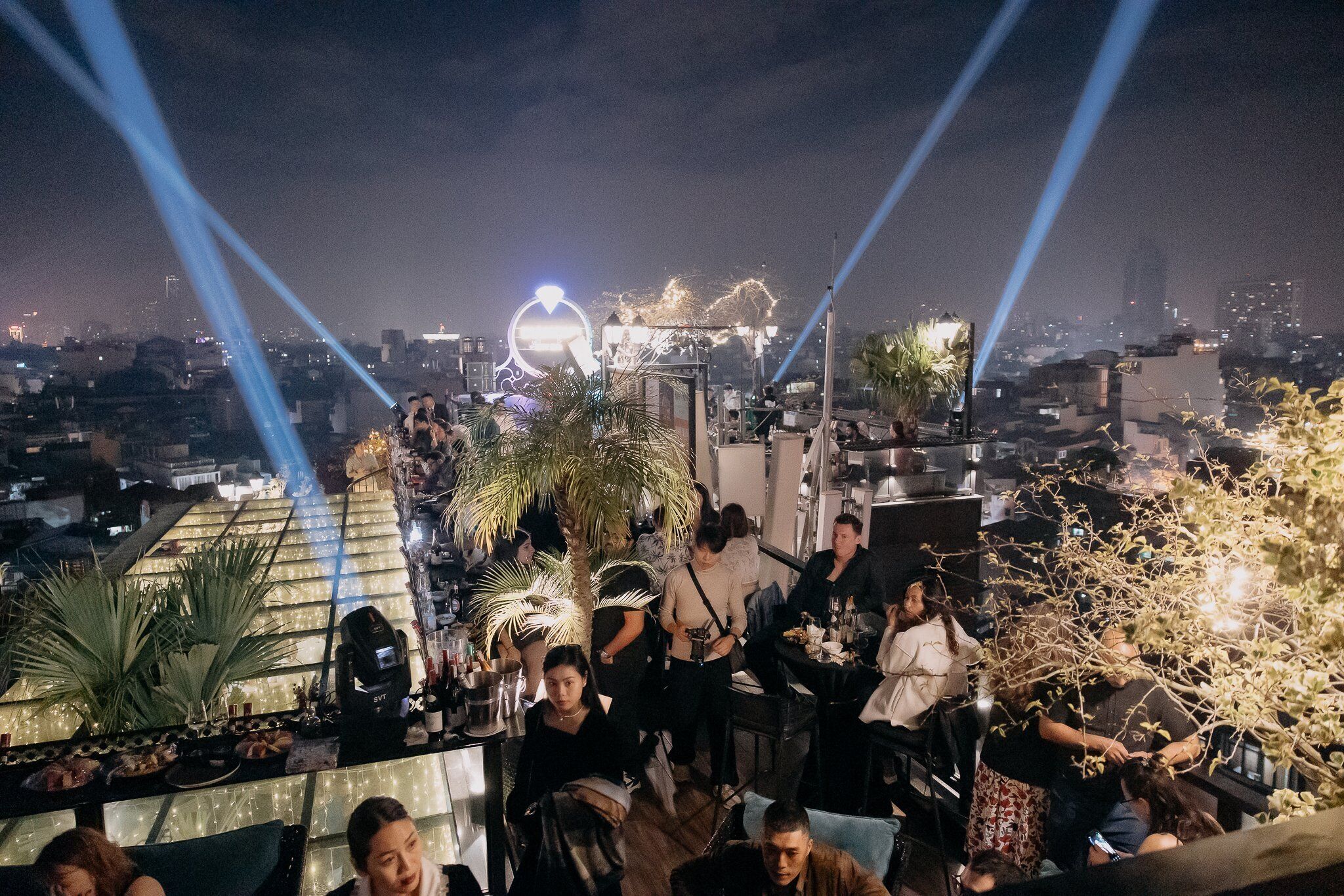 A rooftop bar with a view of the city skyline, illuminated by spotlights.