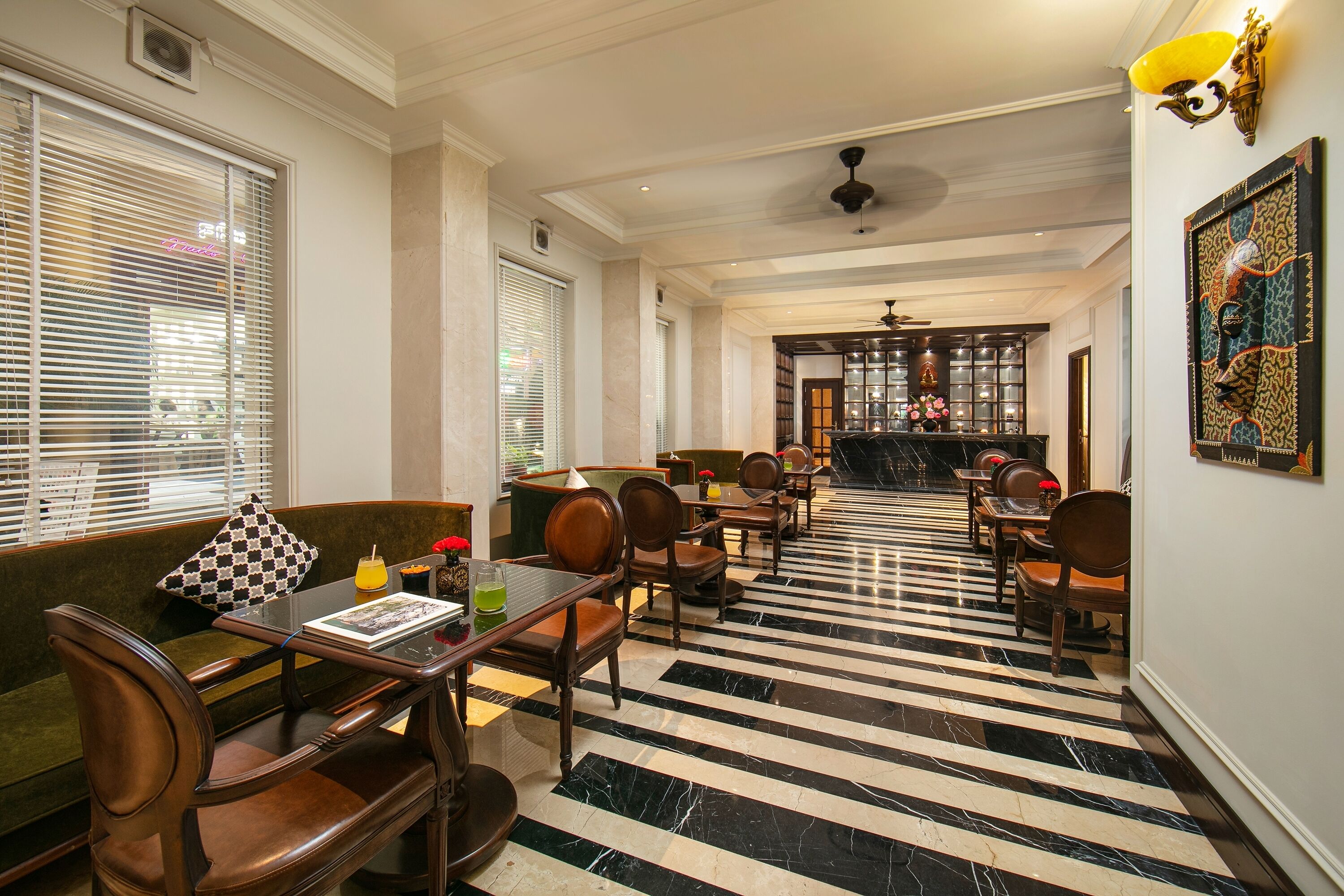 A hotel lobby with a checkered floor, seating area with a sofa and chairs, a bar area with a counter, and a ceiling fan.