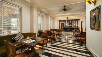 A hotel lobby with a checkered floor, seating area with a sofa and chairs, a bar area with a counter, and a ceiling fan.