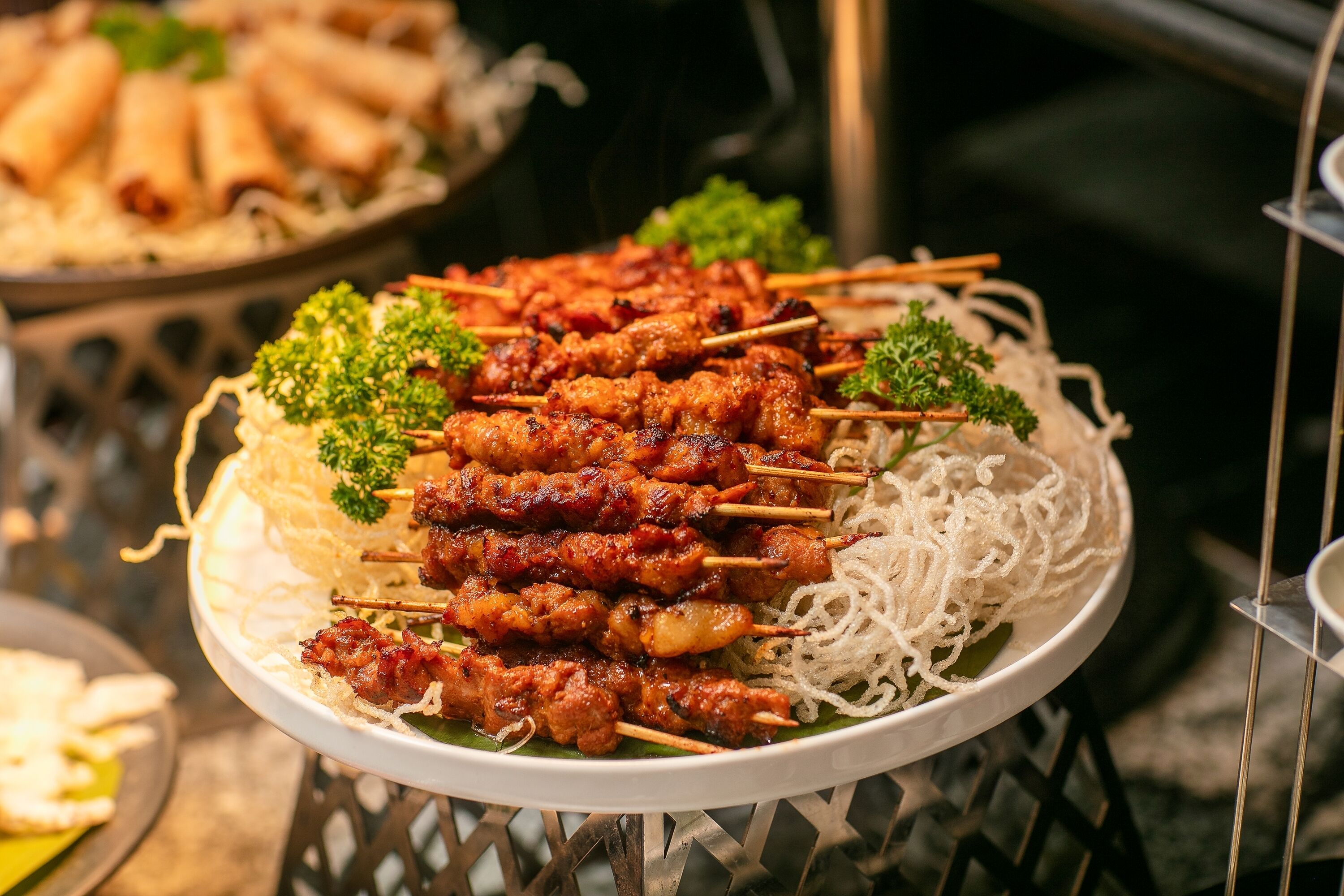 A plate of skewered meat garnished with parsley, served with rice noodles.