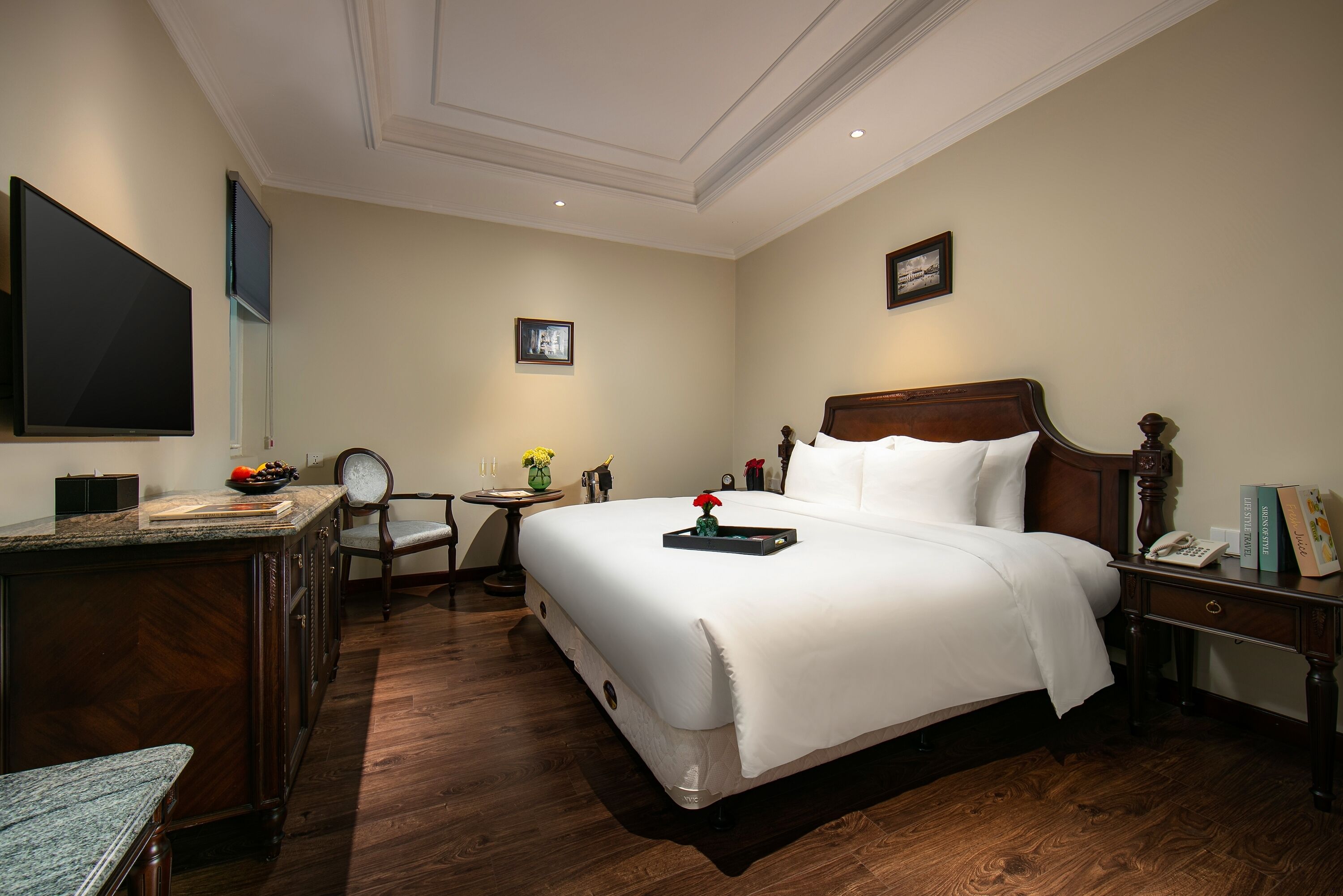 Habitación de hotel con una cama grande, un escritorio con computadora, una silla, una pequeña mesa con un jarrón de flores y un cuadro en la pared.