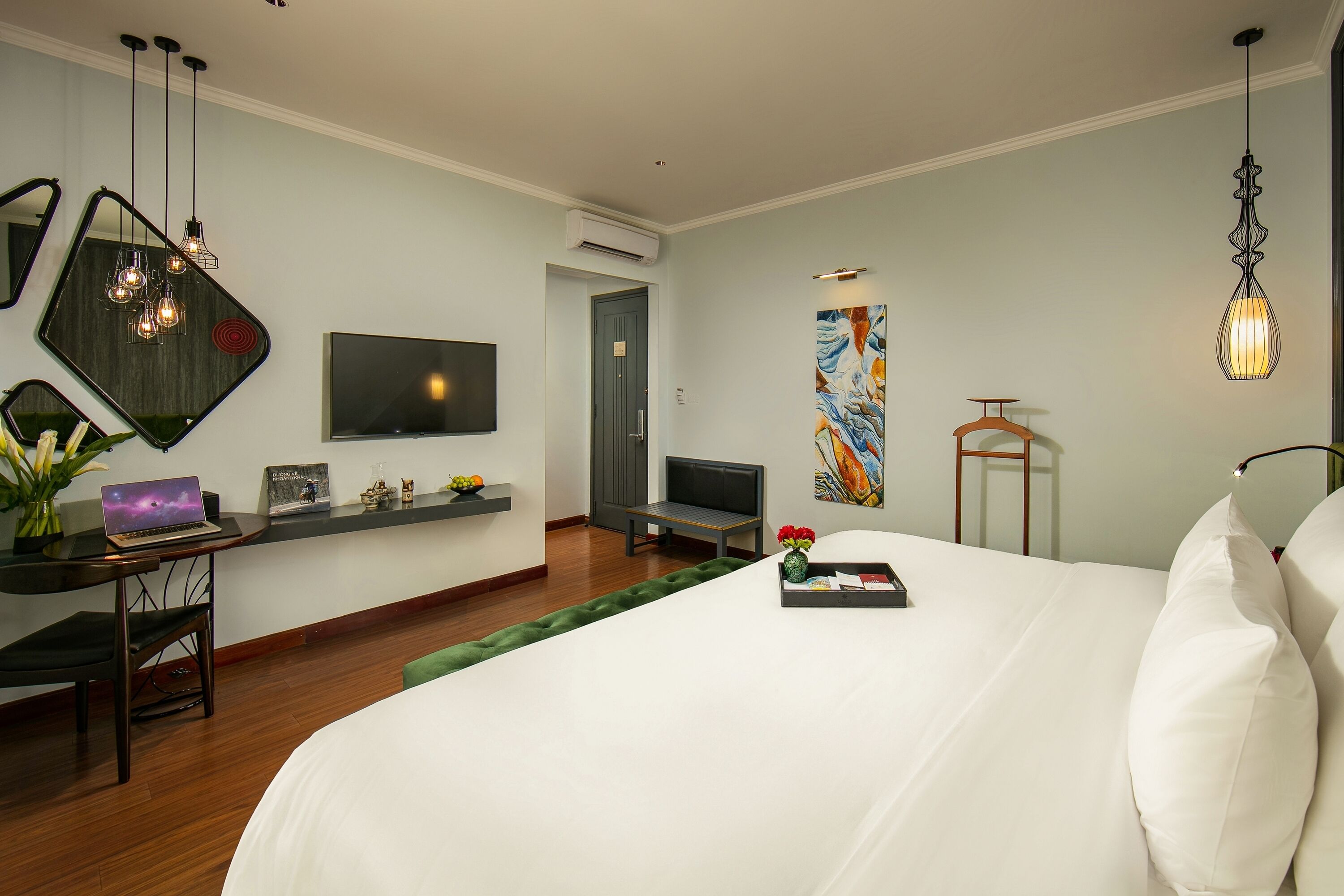 A modern hotel room with a large bed, a desk with a laptop, a flat-screen TV, and a painting on the wall.