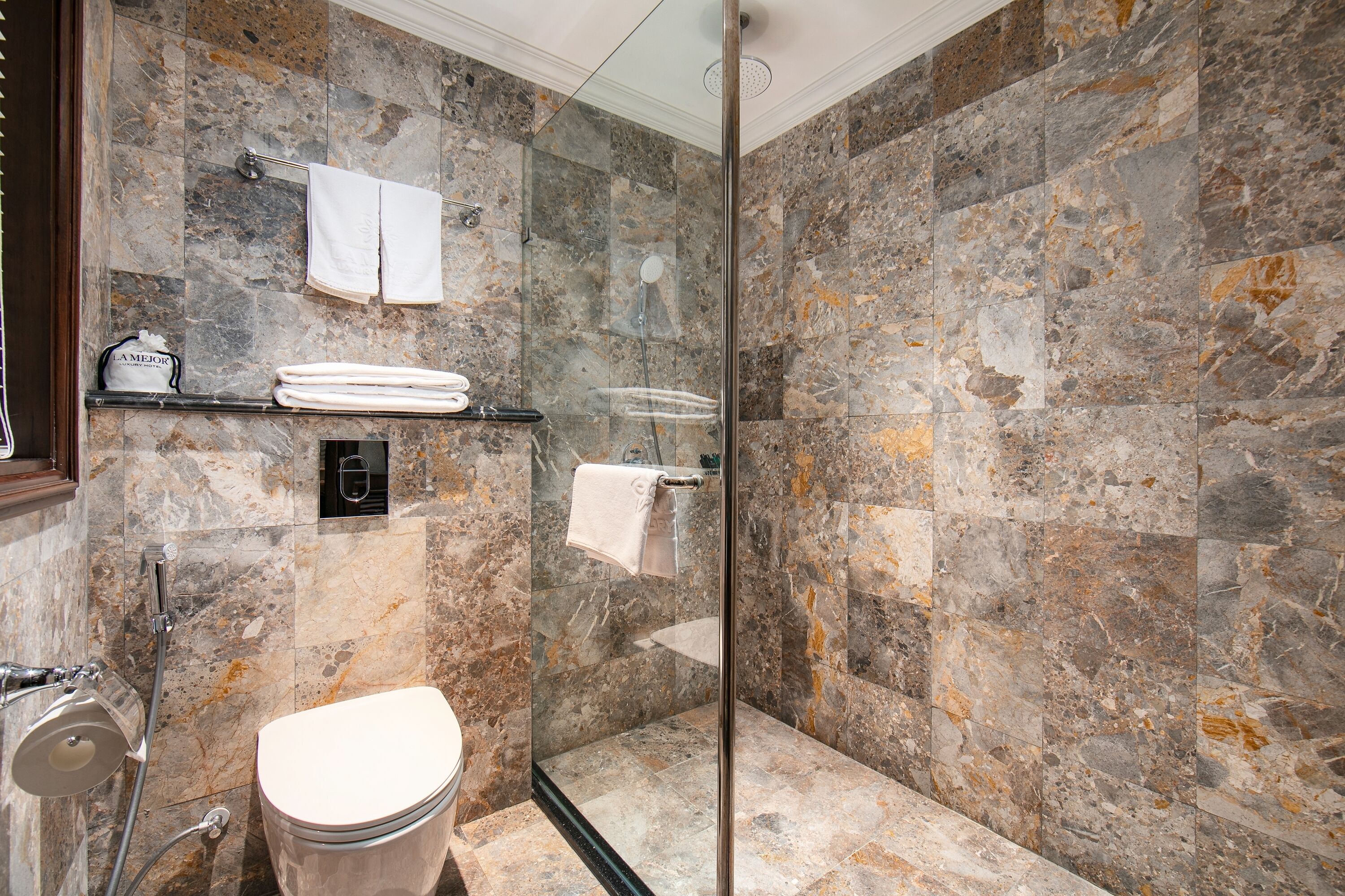 Une salle de bain moderne avec une douche à parois de verre, des murs en marbre et des toilettes.