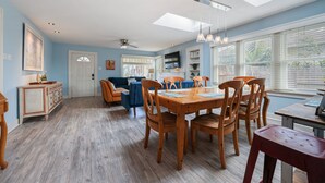 A spacious dining area with a wooden table and chairs, a ceiling fan, and a large window with blinds. - 2 br, 2 bth, fully fenced home - The Sunnyside Up Beach Cottage (Oceanside)