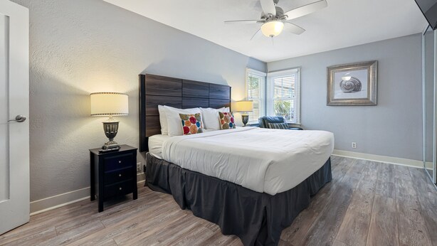 A bedroom with a large bed, a ceiling fan, a nightstand with a lamp, and a window with blinds. - 2 br, 2 bth, fully fenced home - The Sunnyside Up Beach Cottage (Oceanside)