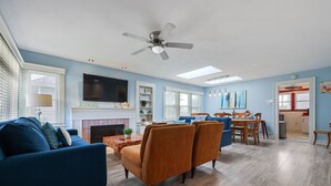 A spacious living room with a blue sofa, a fireplace, and a dining area with wooden chairs and a table. - 2 br, 2 bth, fully fenced home - The Sunnyside Up Beach Cottage (Oceanside)