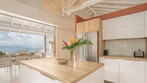 A modern kitchen with a wooden countertop, white cabinets, and a view of the sea.