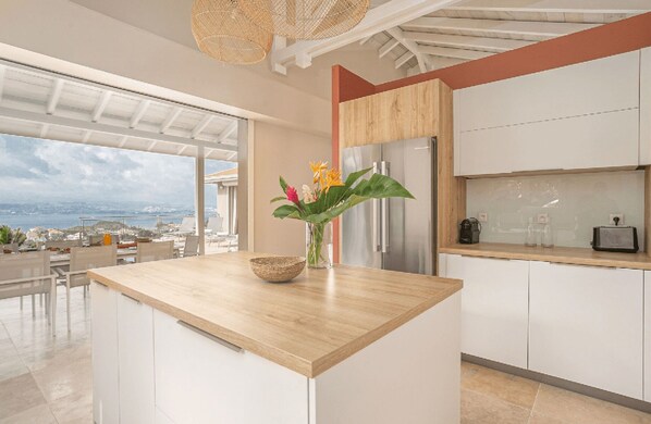 A modern kitchen with a wooden countertop, white cabinets, and a view of the sea. - Tangarane offers two luxury villas with private pools and exceptional views over (LES TROIS ILETS)