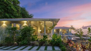 A modern house with a covered porch, surrounded by tropical plants.
