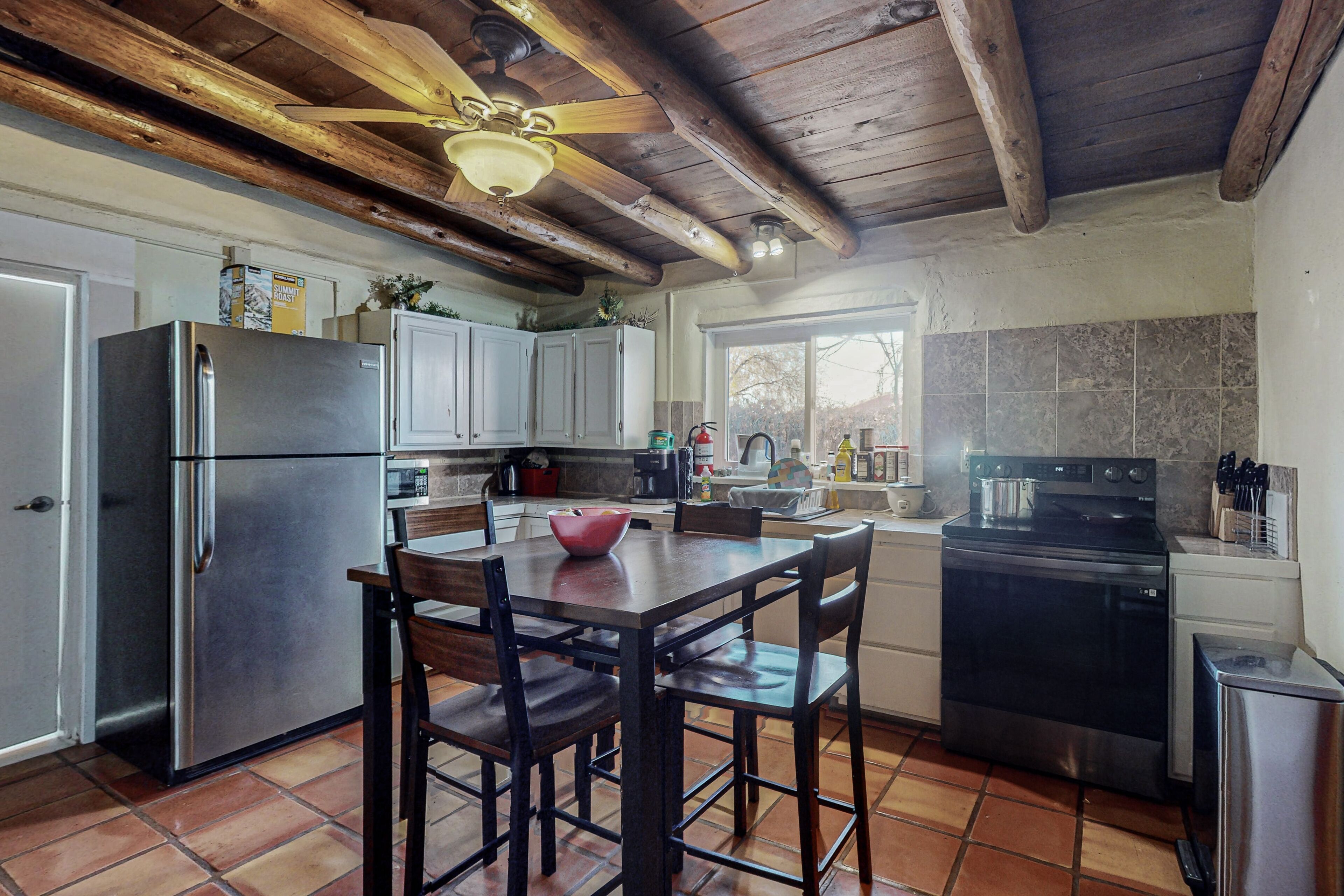 Una cocina con techo de madera, un refrigerador de acero inoxidable, una mesa de comedor con sillas y una estufa.