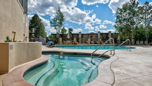 Una piscina con hidromasaje, rodeada de sillones de descanso y un edificio con múltiples ventanales.