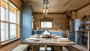 A rustic wooden interior with a large wooden table, benches, a kitchen area, and a sign labeled "Kitchen."