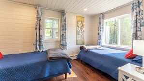 A room with two beds, wooden floors, a window with curtains, and a wall with a painting. - Yacht Club cabin on Burntside, with sauna (Ely)