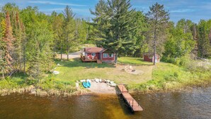 A cabin with a deck, surrounded by trees and a lake. - Yacht Club cabin on Burntside, with sauna (Ely)