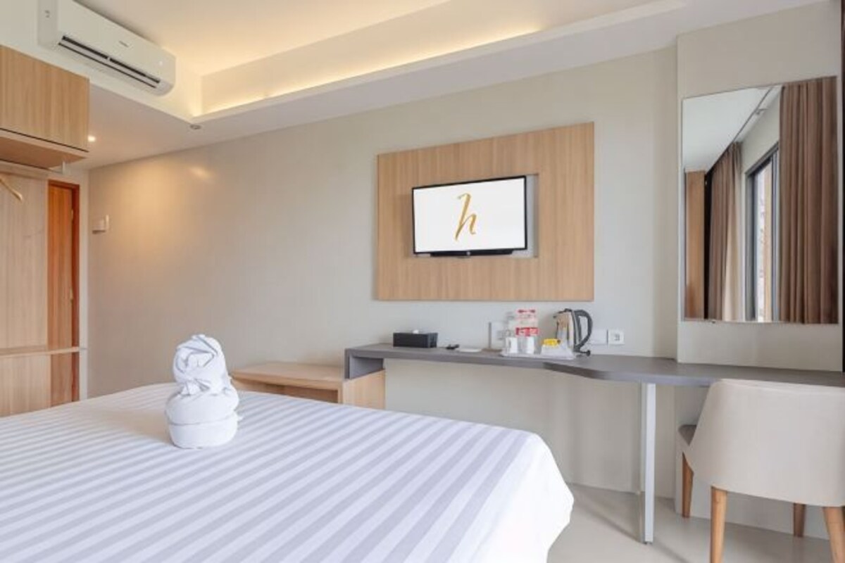 A hotel room with a bed, a desk, a chair, a TV, and a mirror.