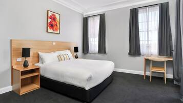 Ein modernes Hotelzimmer mit einem großen Bett, Nachttischen, einem Schreibtisch und einem Fenster mit Vorhängen.