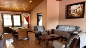 Une pièce chaleureuse avec une table de billard, deux fauteuils, un canapé et un tableau au mur.